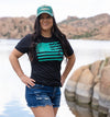Woman by watson lake in arizona in jean cut off shorts and a teal gun flag t shirt in black with a teal hat