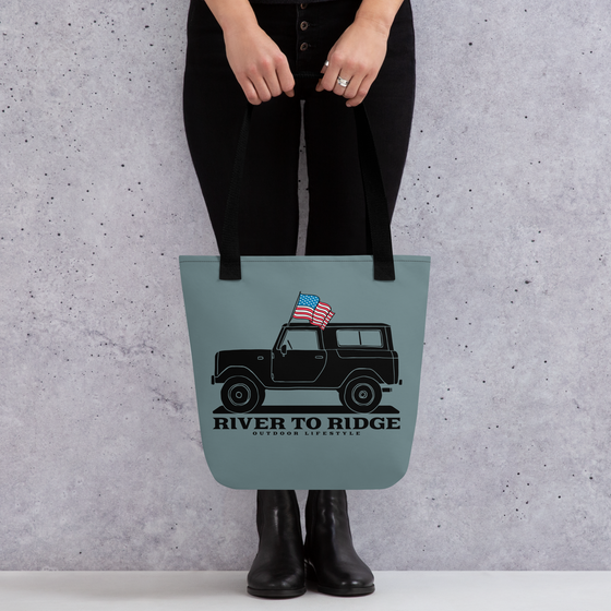 Vintage USA Logo Tote Bag in indigo blue from River to Ridge Clothing Brand. Features a drawing of a vintage bronco truck with an american USA flag - woman in black holding the purse