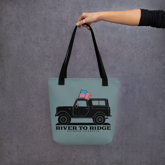 Vintage USA Logo Tote Bag in indigo blue from River to Ridge Clothing Brand. Features a drawing of a vintage bronco truck with an american USA flag - woman holding the purse out with her arm