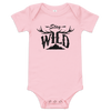 Stay Wild Logo on a baby one piece in pink and the logo has elk antlers on it and a mountain, onesie