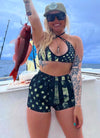 Woman fishing for snapper on a boat wearing a Camo Flag bikini and shorts, long blonde hair and sunglasses. Patriotic swimwear