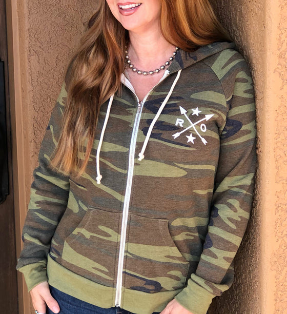 red haired woman wearing a camo zip up hoodie with rockstarlette arrow logo on it