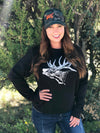 Woman with red hair wearing an elk logo pullover sweatshirt in black and white and a camo hat with the WILD logo on it in orange with elk antlers
