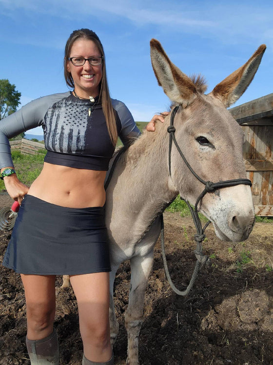 Woman on farm with donkey wearing patriotic 2A grey an black crop top and skirt and muddy boots