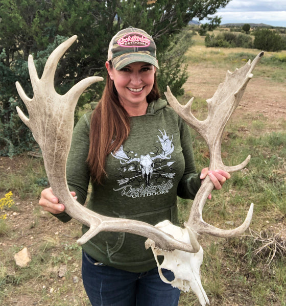 Woman holding taxidermy of a fallow deer antlers with a green hoodie with a moose and arrows on it for Rockstarlette Outdoors