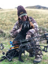Woman on an archery hunt with her bow and a hunting dog wearing a WILD antler beanie and camo from River to Ridge Brand