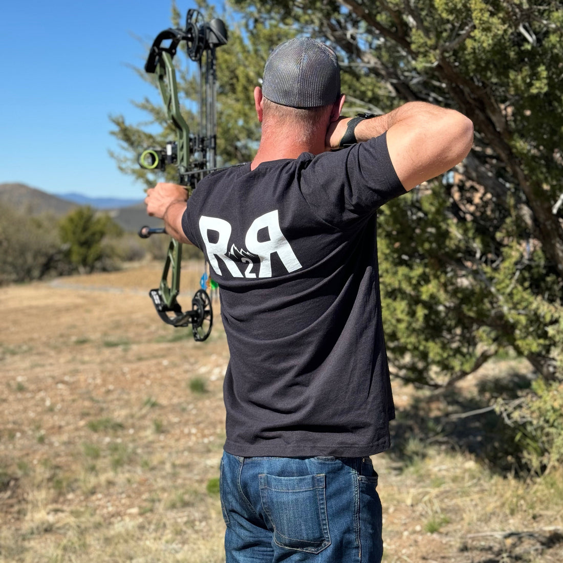  Man shooting a compound bow and arrow in jeans and a R2R T shirt from River to Ridge Clothing Brand