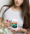 woman with long brown hair holding a coffee mug that says I love adventure and coffee and it has a drawing of mountains and a river and a camping tent