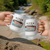 two people cheersing with 2 coffee mugs at a river outdoors and the mugs have an alaska bush plane, small airplane otter on them with the brand name River to Ridge