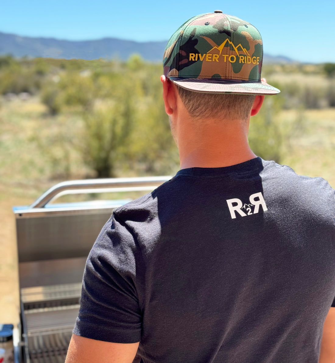  Man wearing a camo flat bill hat from River to Ridge Clothing Brand outdoors