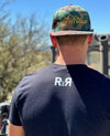 Man wearing a camo flat bill hat from River to Ridge Clothing Brand outdoors
