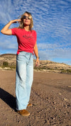 woman standing on a dirt road in new mexico wearing an elk logo t shirt and high waist jeans and crocs