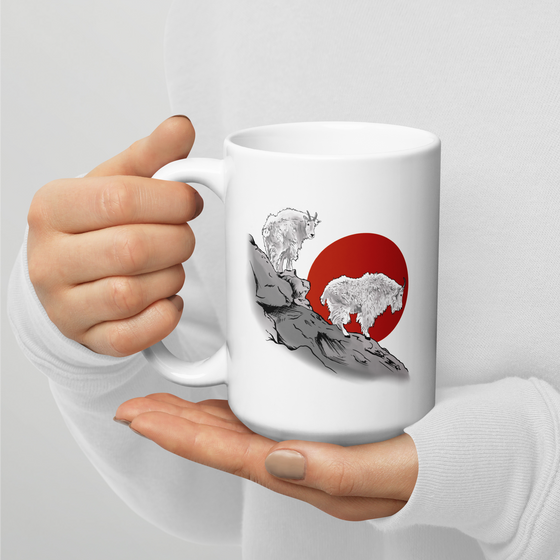 close up of a person holding a coffee mug that is large with 2 mountain goats on it standing on a cliff with a red sun