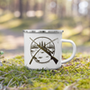 Hunting & Fishing Logo Enamel Camping Coffee Mug from River to Ridge Brand with a fishing rod and a rifle crossed over a river scene, mug sitting in the forest in the moss