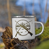 Hunting & Fishing Logo Enamel Camping Coffee Mug from River to Ridge Brand with a fishing rod and a rifle crossed over a river scene, mug sitting on a log in the forest