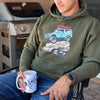 Elk Logo Coffee Mugs from River to Ridge Brand - man holding it on the patio outside and wearing an olive offroading bronco hoodie