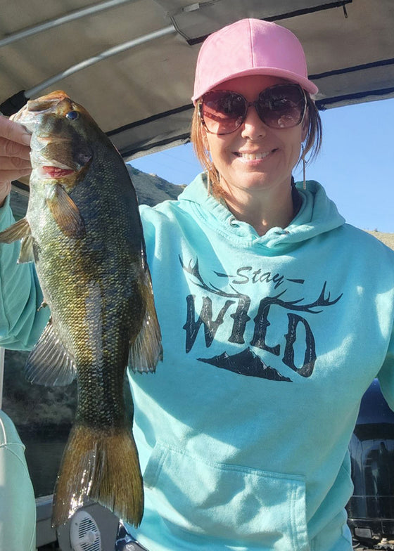 Woman bass fishing in a stay wild mint teal hoodie from River to Ridge Brand, holding up a large bass