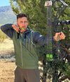 Man shooting a compound archery bow at full draw wearing a tactical logo zip up hoodie in olive and grey with rifles on it from the Brand River to Ridge Clothing