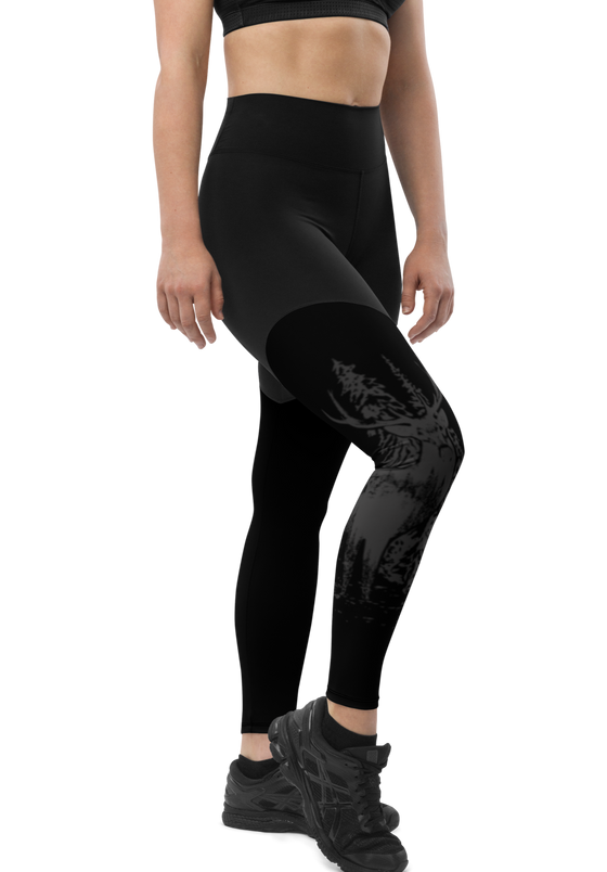 Woman's leggings in black with woodland elk deer design on them, she is wearing a black top and black shoes