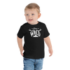Little boy wearing a toddler t shirt and jeans. The t shirt is from river to ridge brand and is black with a white stay wild logo on it with elk antlers and a mountain