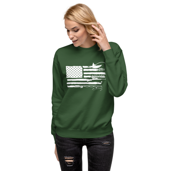 Blonde woman wearing jeans and a sweatshirt in green with the River to Ridge Brand Sportsmans Flag Logo on it, in white with an American Patriotic USA flag and the stripes have bass fishing, fly fishing, duck hunting, elk antlers, shooting in the stripes