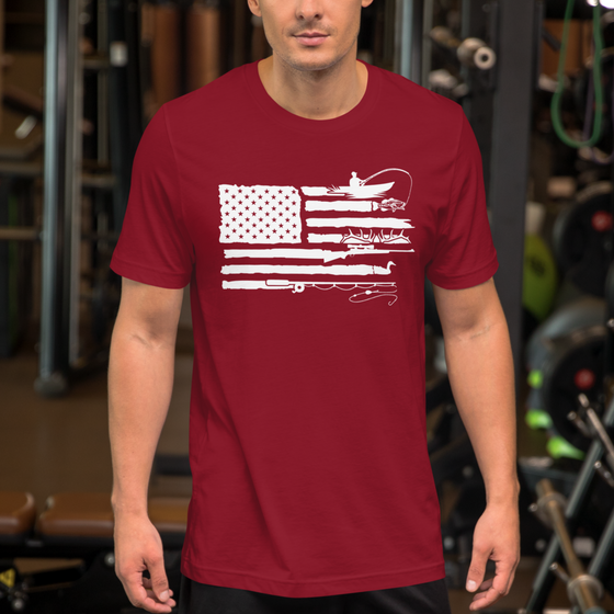 man wearing a sportsmans flag bred t shirt from River to Ridge Clothing Brand at the gym. shows a USA flag with the stripes replaced by kayak fishing for bass, antlers, goose hunting, fly fishing drawings