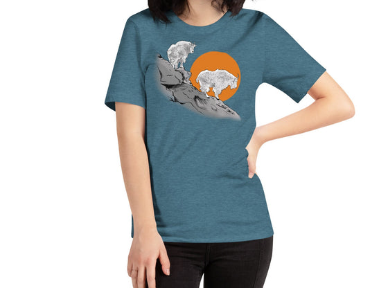 woman with dark hair wearing a turquoise t shirt with mountain goats on it standing on a cliff