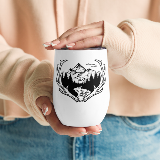 Woman holding a wine tumbler for camping that is metal and white with a lid and it says Adventure Awaits and the River to Ridge Logo with Mountains and elk antlers