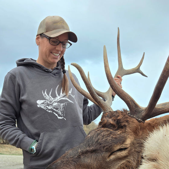 woMan standing next to a large deer with antlers, outdoors.
