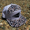A snapback cap with a brown and black camo pattern on the front panels and brim, and a white perforated back. It features a light gray visor with a black patch that reads 'GENESIS 27:3'.