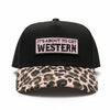 A black trucker hat with a pink leopard print brim and a white patch reading 'IT'S ABOUT TO GET WESTERN', photographed outdoors on a wooden surface.