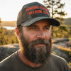 Man wearing a cap with 'Hunting Fishing Freedom Faith' text in a natural setting