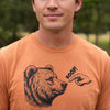 A close-up of a person wearing a heathered orange crewneck t-shirt with a black graphic of a bear's head and a pointing hand saying 'BOOP!'.