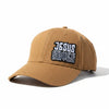 A tan baseball cap with a black and white embroidered patch reading 'JESUS SAVES' resting on a stone pillar outdoors.