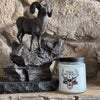 Jar of candle on a stone surface with a decorative metal goat figure