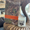 Camouflage-covered Bible and a candle with a deer design on a textured surface.