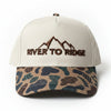 A baseball cap with an off-white front panel and a beige, navy, and dark brown camouflage patterned visor, featuring a black embroidered 'RIVER TO RIDGE' logo on the front.