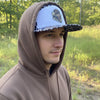 Cap with camouflage brim and white visor featuring a dog and duck design on a textured surface.