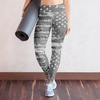 Woman holding a yoga mat wearing a white sports bra and star-patterned leggings against a plain wall.