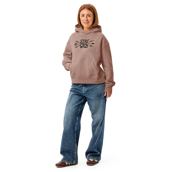 Person wearing a brown hoodie with 'Stay Wild' text and blue jeans on a white background