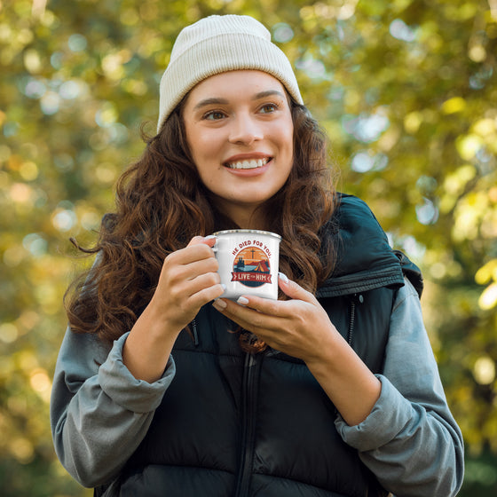 Product mockup of a Christian enamel camping mug from River to Ridge clothing brand featuring the saying "he died for you, live for him" and a camping scene in red and orange and blue