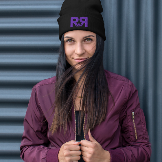 Product mockup of a River to Ridge Logo Beanie in black with purple stitching R to R on a woman with long hair wearing a purple jacket