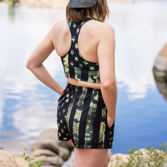Woman at the lake wearing a Camo Flag Sports Bra and Shorts with pockets, athletic, backwards hat Rockstarlette Outdoors