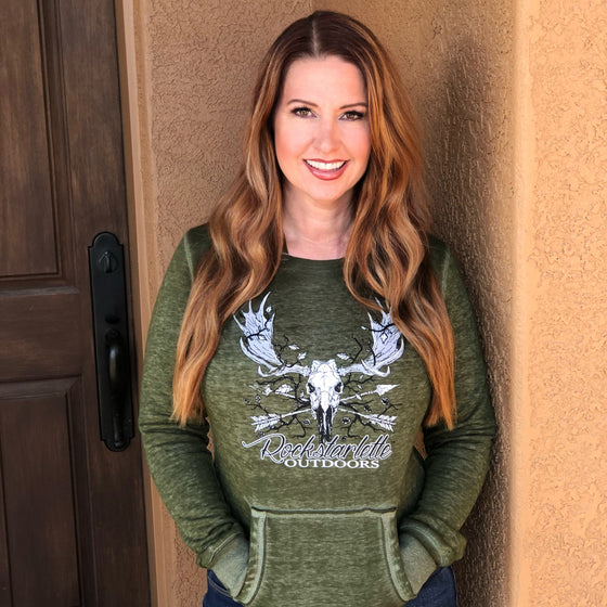 Woman with red hair wearing a Rockstarlette Outdoors hoodie in green with a moose and archery arrows on it, bowhunting