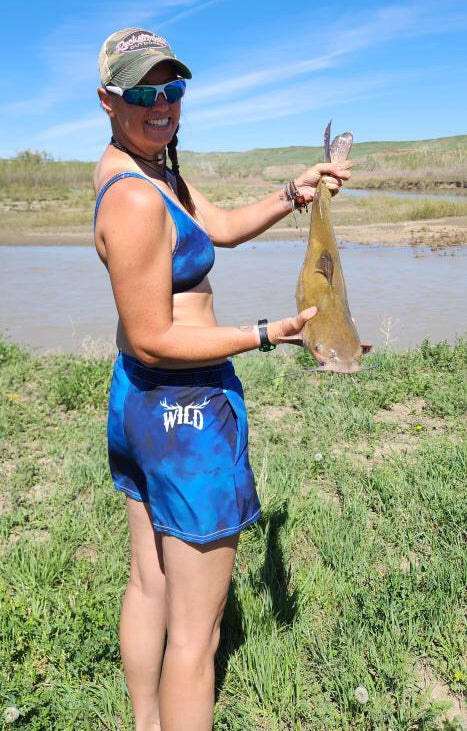 woman fishing for carp and wearing a watercolor bikini top and bottom in blue with the elk antler wild logo on the back hip
