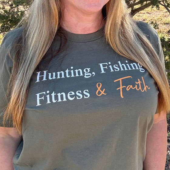 Person wearing a t-shirt with text 'Hunting, Fishing, Fitness & Faith' outdoors.