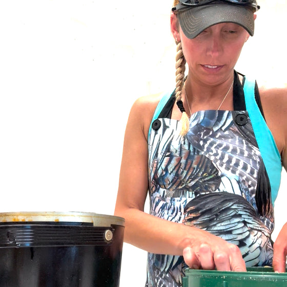 Person wearing a patterned apron and cap, working with a large black container on a white background