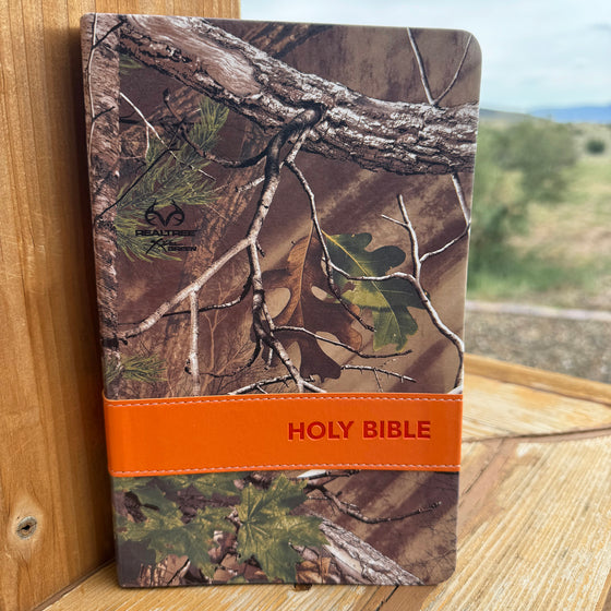 Camouflage-patterned Bible with orange strap on a wooden surface