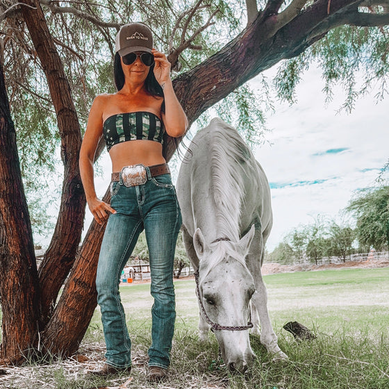 Woman in outdoor setting with a horse, wearing a camouflage top and jeans.