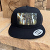 Black trucker cap with a forest design on a wooden surface